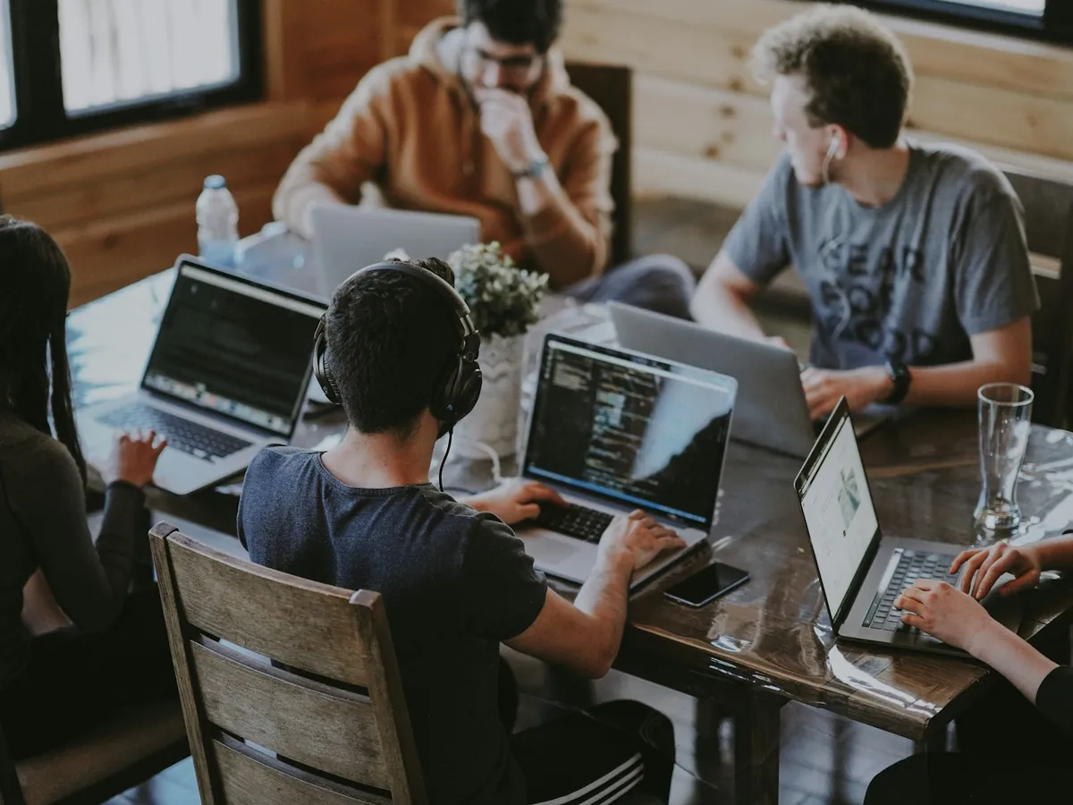 A team of developers working together on laptops around a wooden table